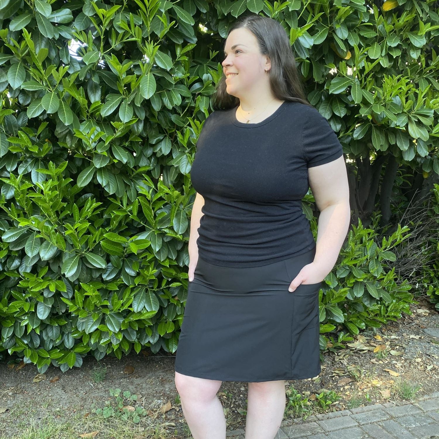Woman wearing a black skirt standing in front of green bushes