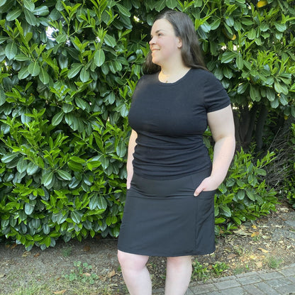 Woman wearing a black skirt standing in front of green bushes