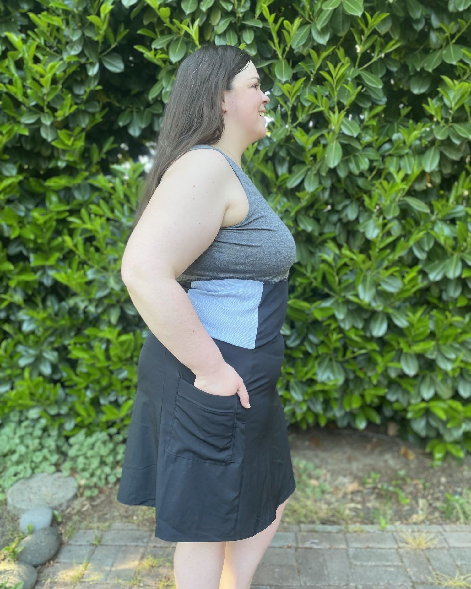 Woman wearing a gray and black dress standing in front of green bushes.