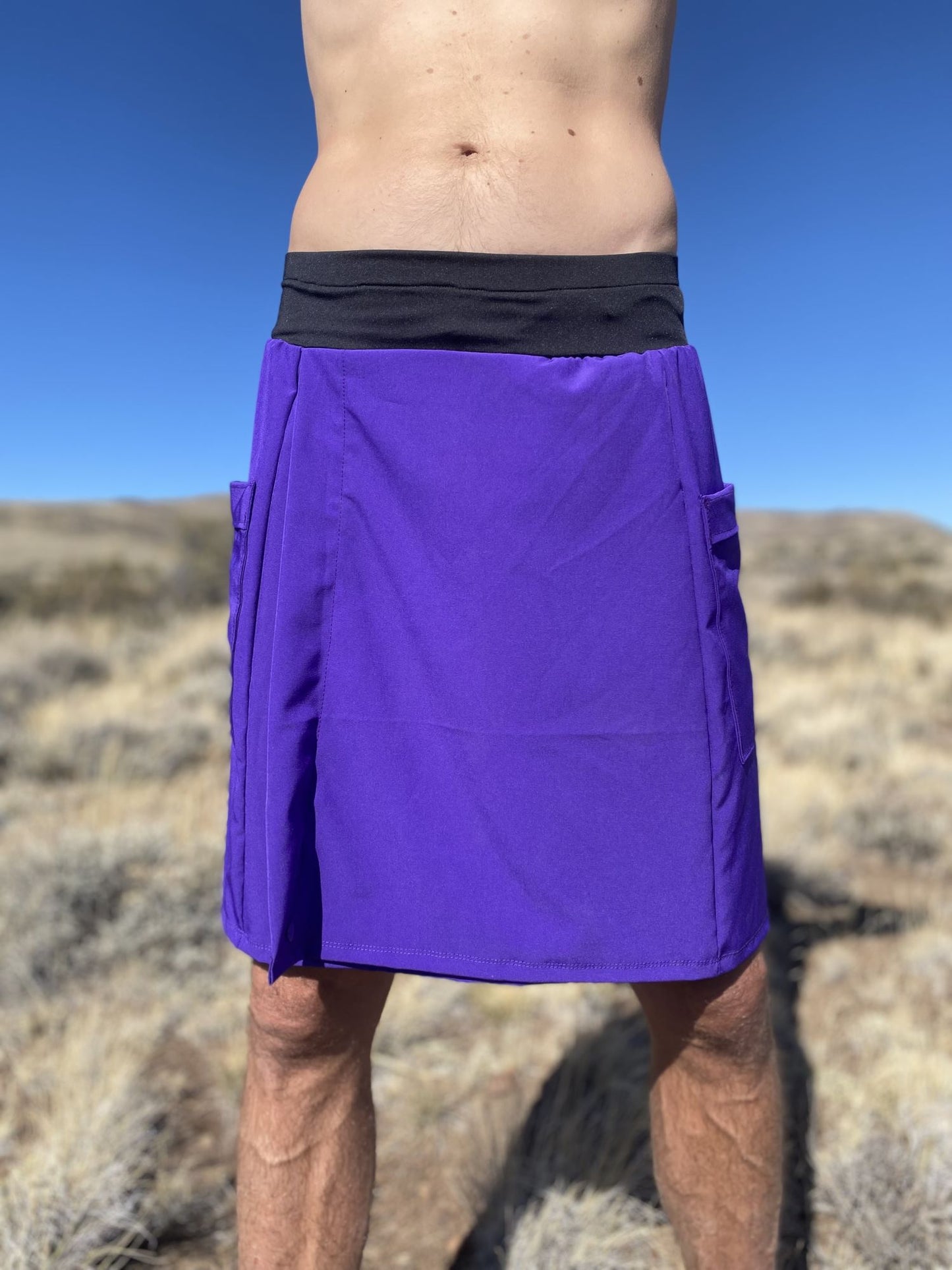 Person wearing a purple rain kilt with a black waistband in a desert setting.