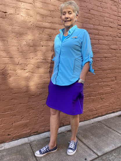 Person wearing a blue shirt and purple skirt standing against a brick wall.
