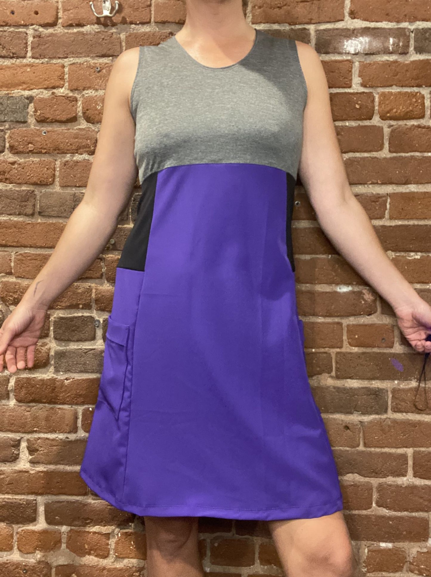 Person wearing a gray and purple dress against a brick wall