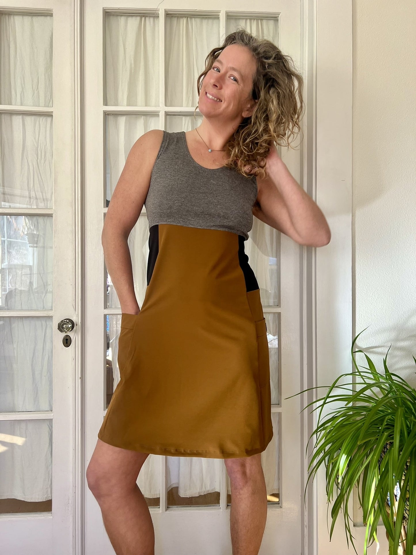 Woman wearing a sleeveless dress with a gray top and copper dress indoors.