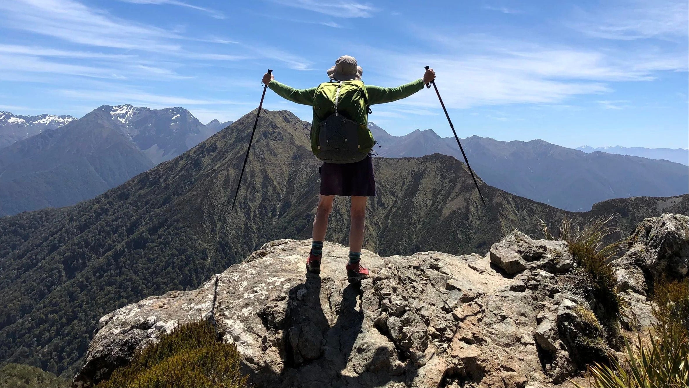 Woman backpacker standing on a top of a mountain looking at wide view of mountains