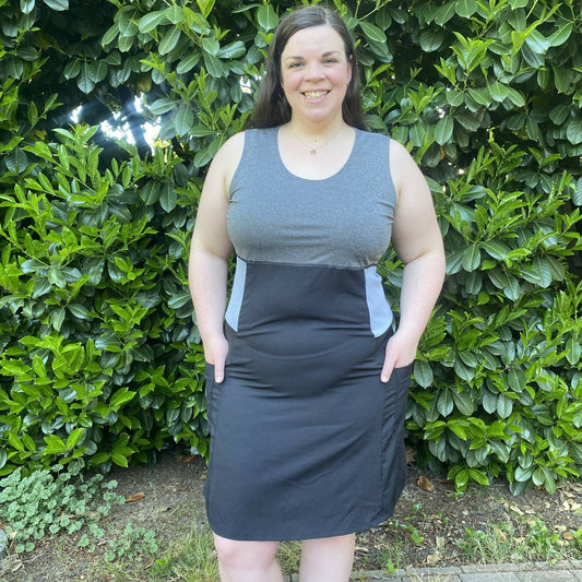 Person wearing a gray dress against a green hedge background