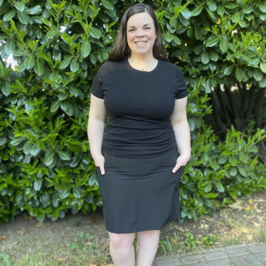 Woman wearing a black top and skirt standing in front of green bushes