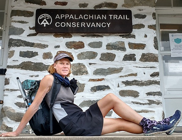 Person sitting on a stone wall with a backpack in front of an Appalachian Trail Conservancy sign.