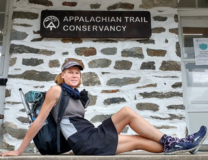 Person sitting on a stone wall with a backpack in front of an Appalachian Trail Conservancy sign.