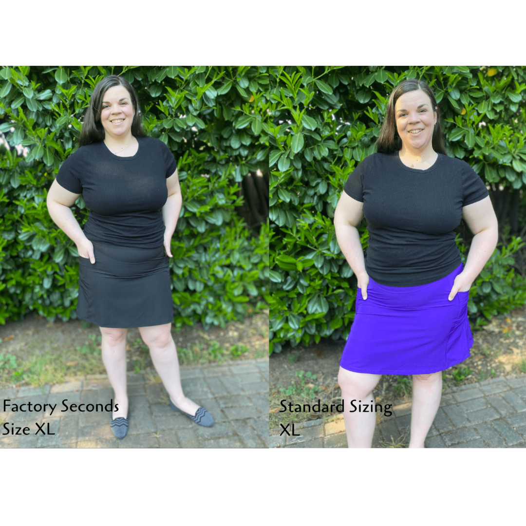 Comparison of a person wearing a black t-shirt and skirt in 'Factory Seconds' and 'Standard Sizing' sizes against a green hedge background.