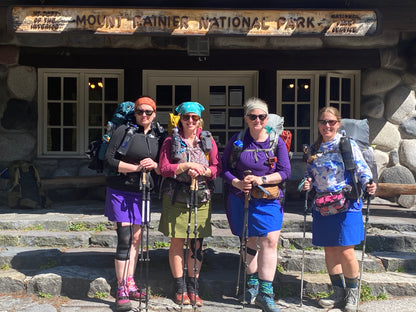 Four hikers with backpacks and sunglasses standing in front of Mount Rainier National Park entrance.