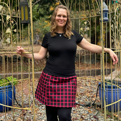 Woman wearing a black top and red plaid skirt standing in front of an ornate metal gate.
